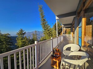Ein Balkon mit Korbstühlen, einem kleinen Tisch mit Flasche und Gläsern sowie Blick auf Berge und Bäume.