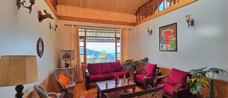 A cozy living room with wooden floors, a red sofa, a patterned armchair, and a wooden staircase.