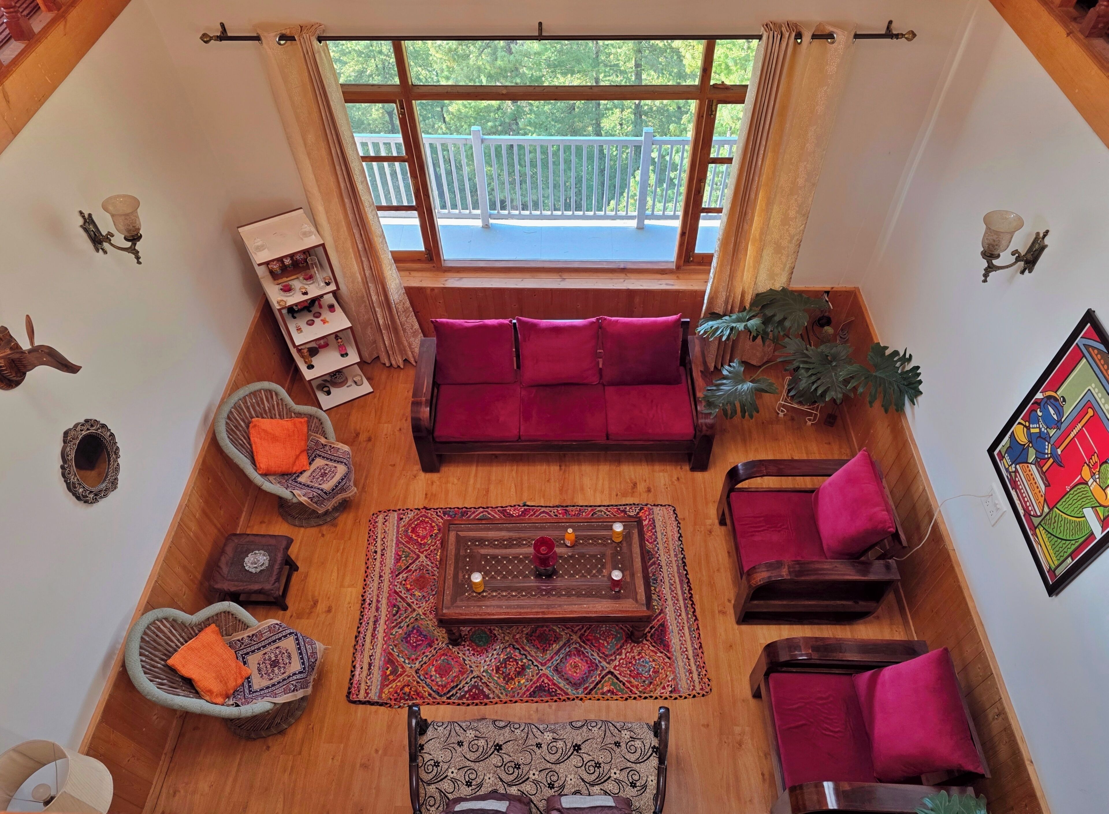 A cozy living room with a wooden floor, a red sofa, a patterned rug, and a balcony with a railing.