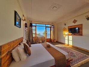A bedroom with a bed, a television mounted on the wall, and a large window with a view of the outdoors. - Kufri Farms (Kufri)