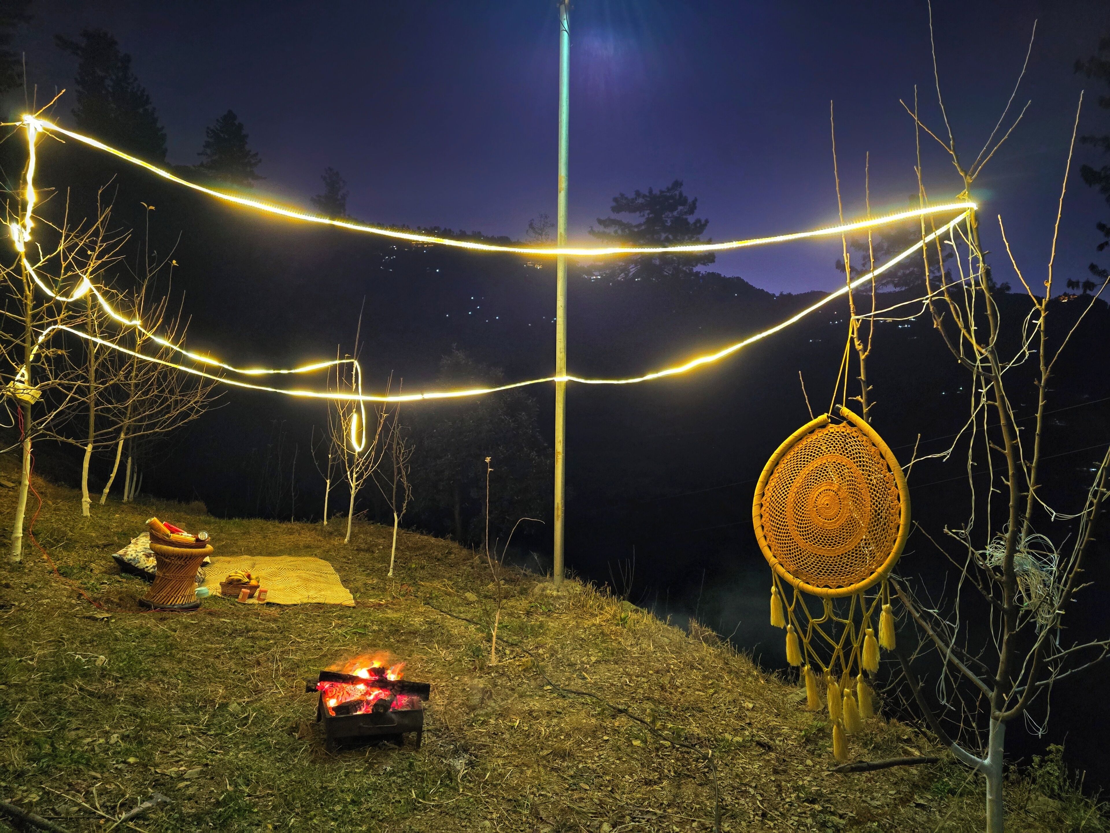 A nighttime outdoor setting with string lights, a fire pit, and a woven chair.