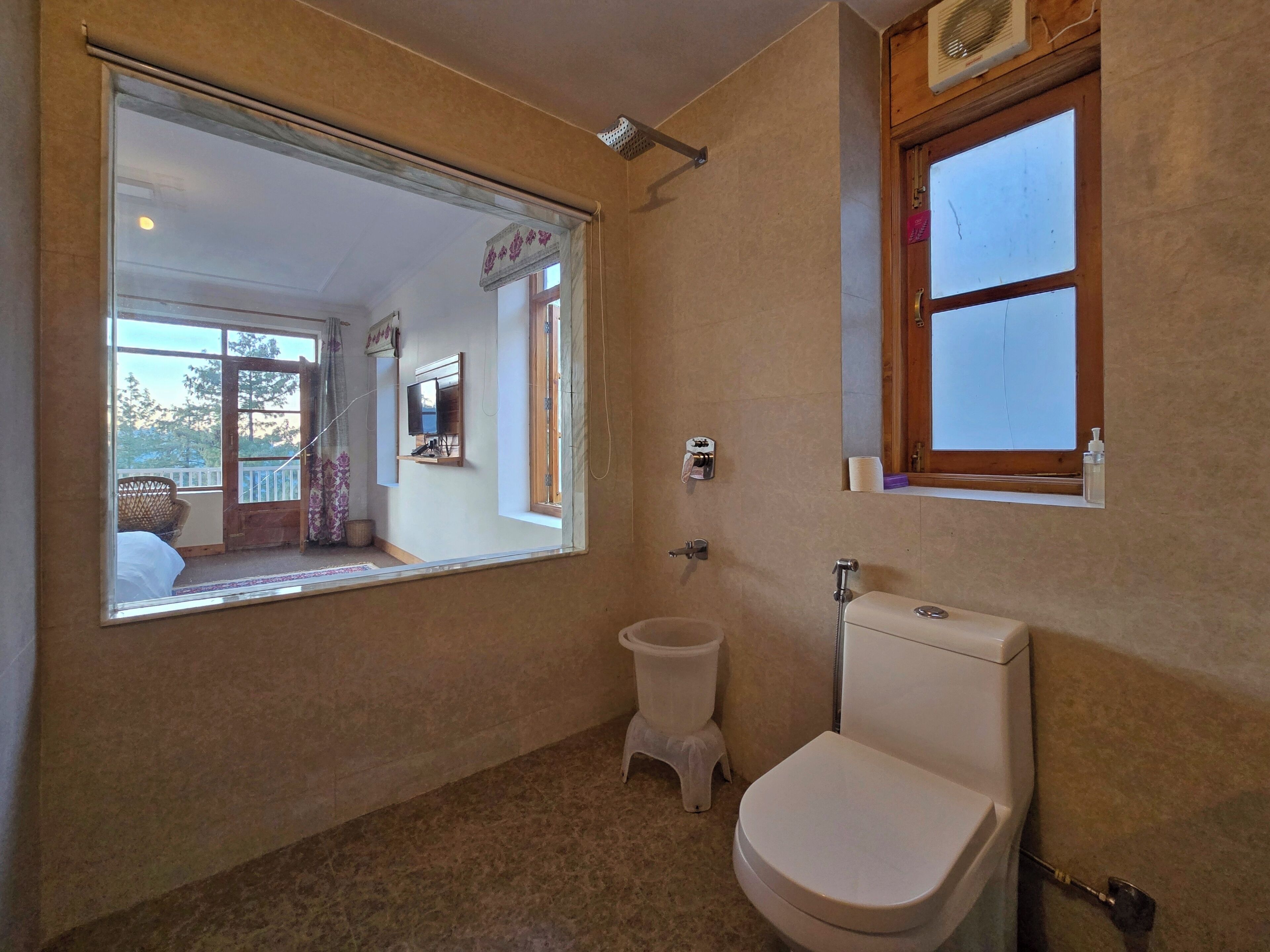 A bathroom with a toilet, bidet, and a large mirror reflecting a balcony with a view of trees.