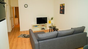 A modern living room with a grey sofa, a flat-screen TV, a small table with a vase, and a painting on the wall.