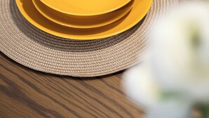 A wooden dining table with a yellow plate and a woven placemat. - Spacious & Cosy APT - Msida Uni Heights (Msida)