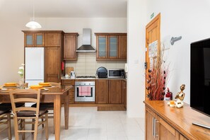A modern kitchen with wooden cabinets, a stove, microwave, and a dining area with chairs and a table. - Spacious & Cosy APT - Msida Uni Heights (Msida)