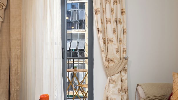 A bedroom with a wooden table, a potted plant, a bed, and a view of the outside through a window with curtains. - Spacious & Cosy APT - Msida Uni Heights (Msida)
