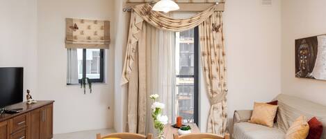 A dining area with a wooden table set for four, a television on a cabinet, and a sofa with cushions.