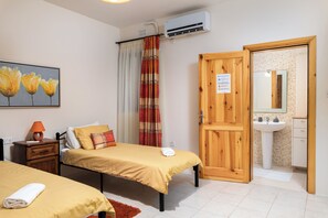 A bedroom with two beds, a wooden door, a bathroom with a sink, and an air conditioning unit. - Spacious & Cosy APT - Msida Uni Heights (Msida)
