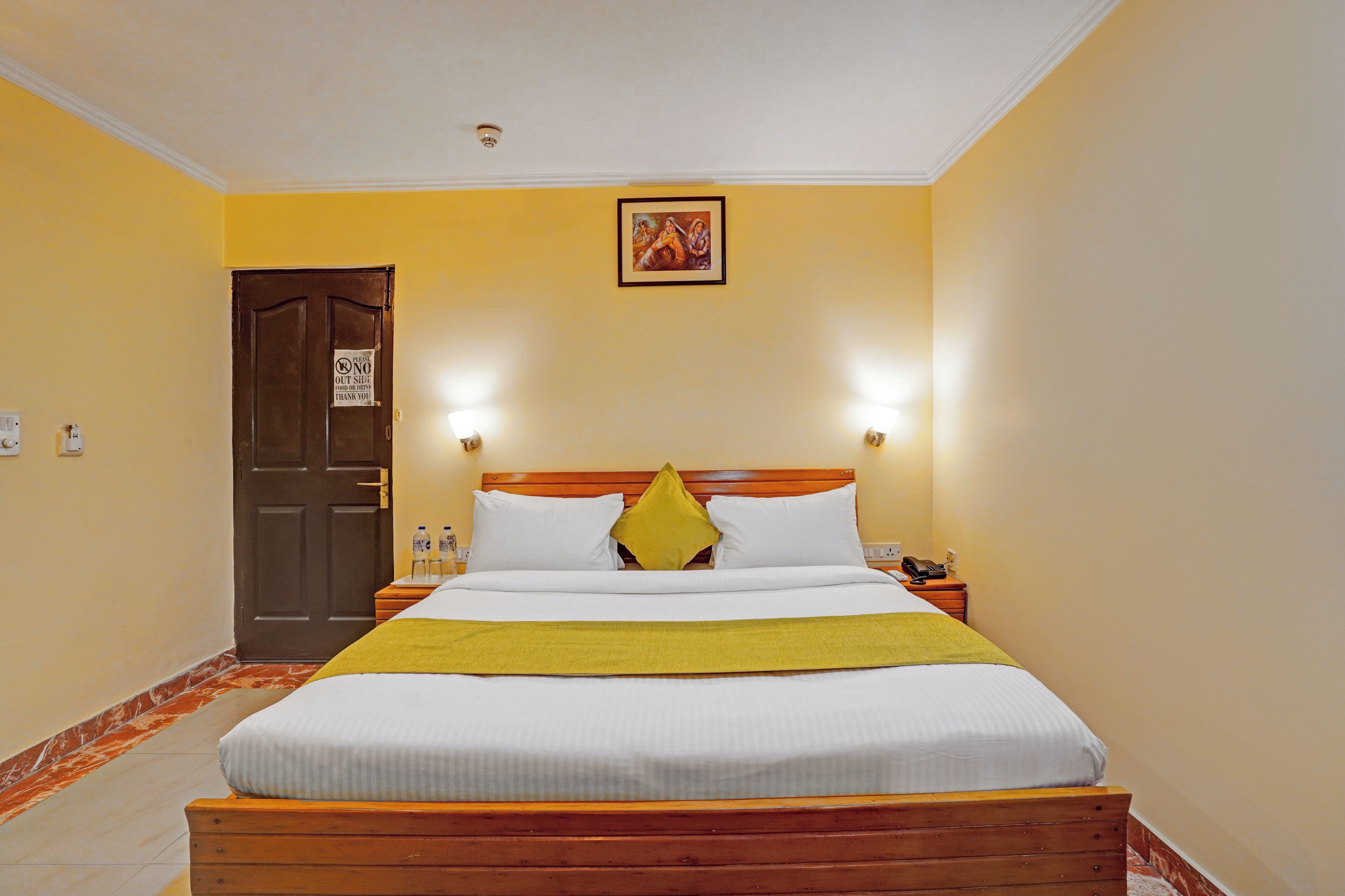 A hotel room with a wooden bed, a yellow wall, and a door with a 'NO OUTSIDE' sign.