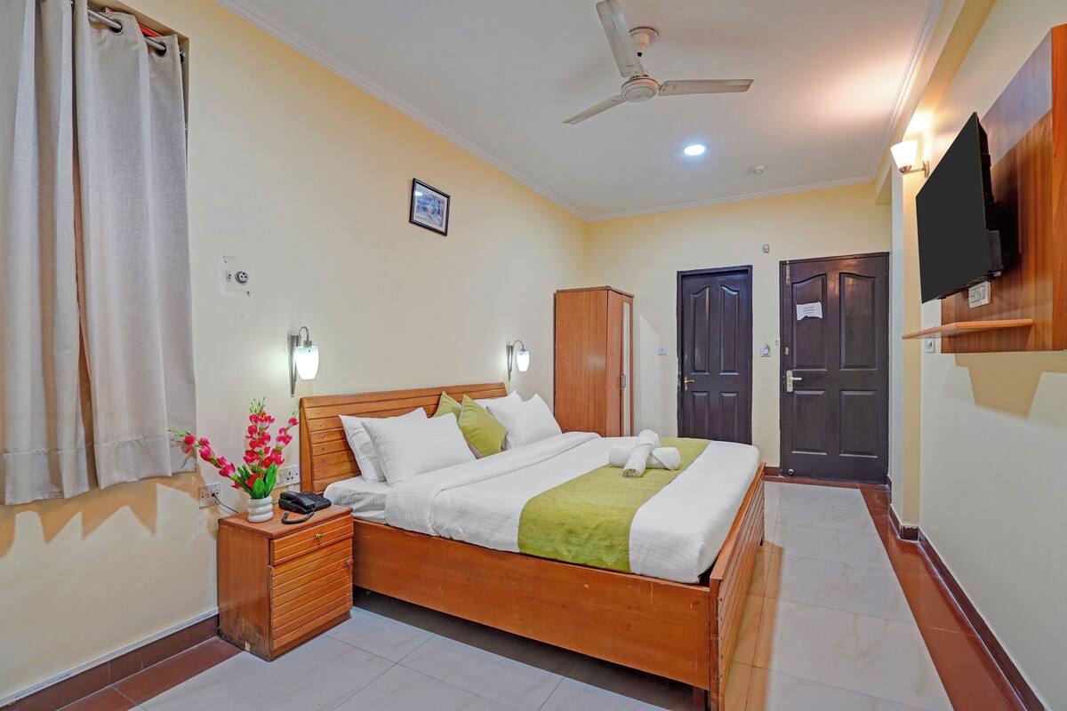 Une chambre d’hôtel bien rangée, avec un lit, une table de chevet, une commode et un téléviseur fixé au mur.