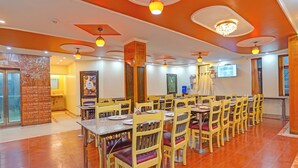 Un vaste espace dédié à la salle à manger, avec plusieurs tables et chaises, un mur en briques apparentes et un plafond agrémenté de luminaires circulaires.