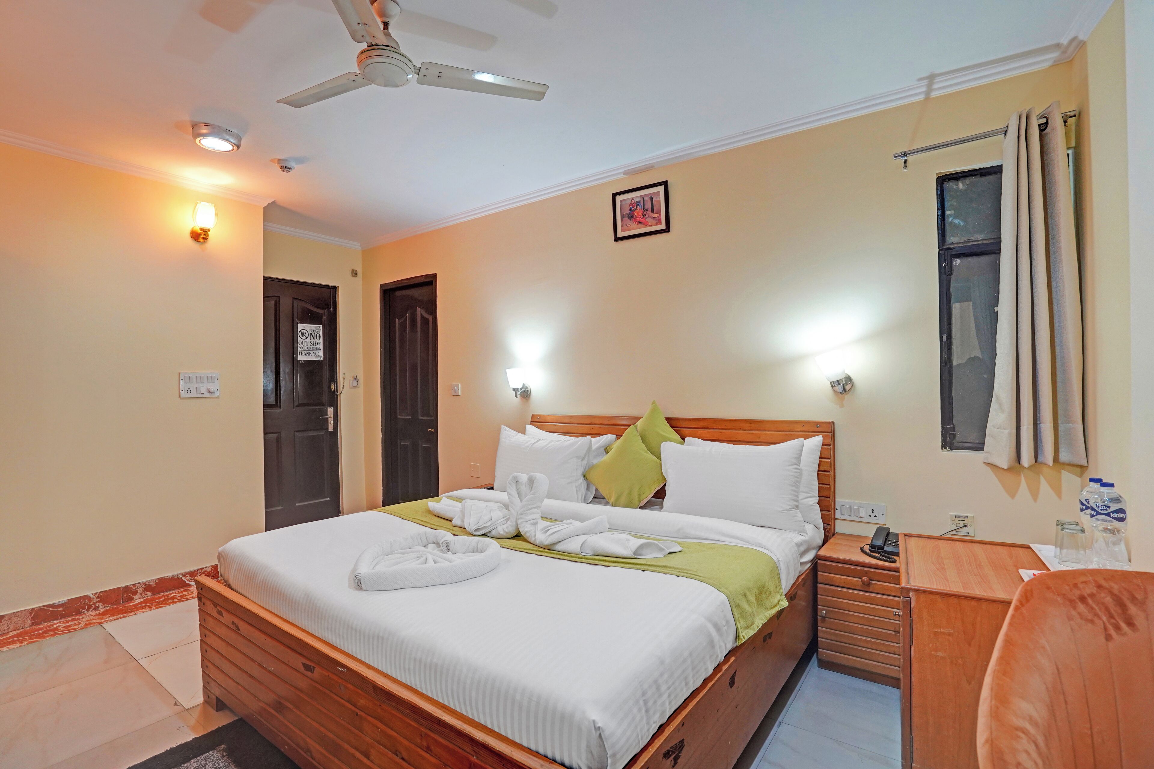 A neatly made bed with white linens and a green throw blanket, a wooden nightstand with a lamp, and a ceiling fan.
