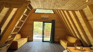 Amplia habitación en el ático con listones de madera en el techo, un sofá, una mesa de comedor y vistas a través de un ventanal.