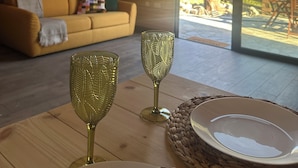 Interior de madera con techo alto, un sofá, dos vasos y vistas por un ventanal.