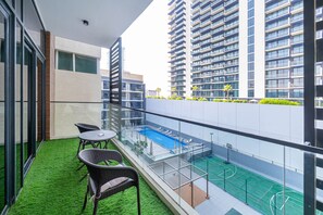 A balcony with artificial grass, a pool, and a basketball court. - Easy Access to Community Parks & Green Spaces,15 minutes drive to Miracle Garden – Rigel, JVC (Dubai)