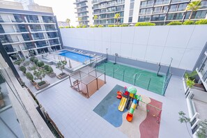 Ein Poolbereich auf dem Dach mit Basketballfeld, Spielgeräten und Topfpflanzen.