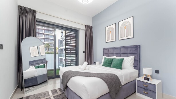 Quarto moderno com uma cama grande, mesa de cabeceira, espelho e vista para o exterior.