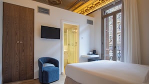 Ein Hotelzimmer mit einem großen Bett, einem blauen Sessel, einem an der Wand befestigten Fernseher und einem Holzschrank.