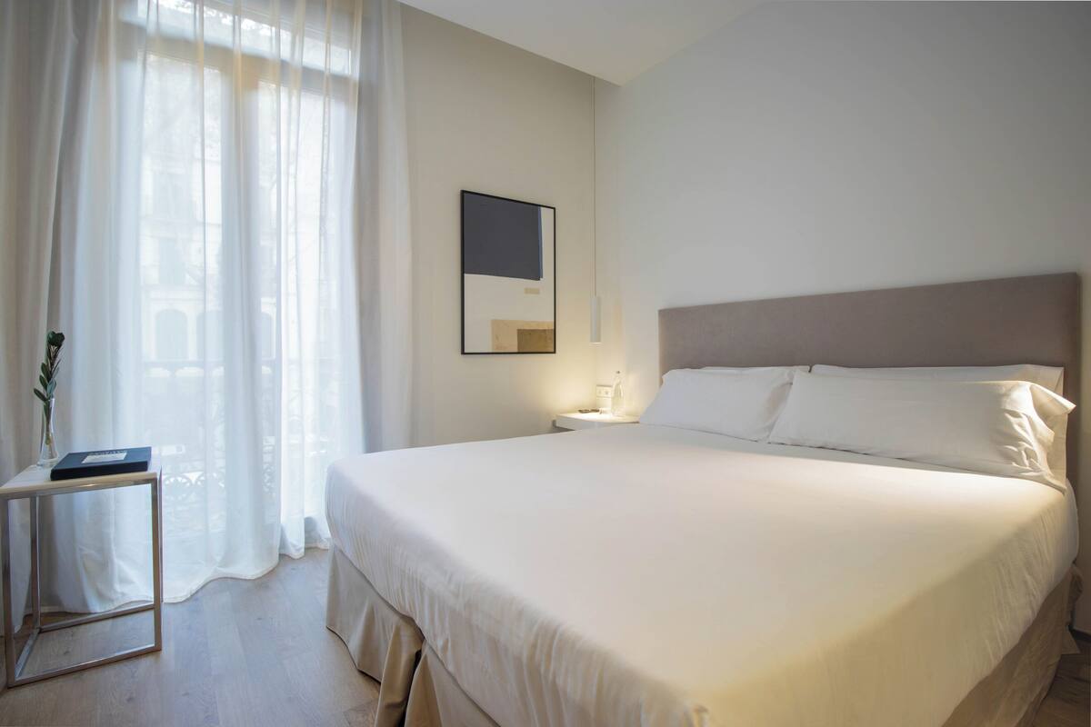 Un letto ben rifatto in una camera d'albergo, con un comodino, una lampada e un quadro appeso al muro.