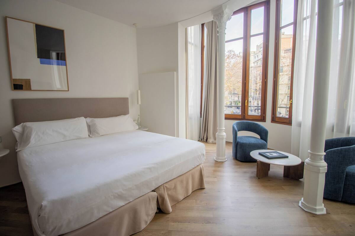 Una camera d'albergo con un letto grande, un tavolino rotondo e una poltrona blu.