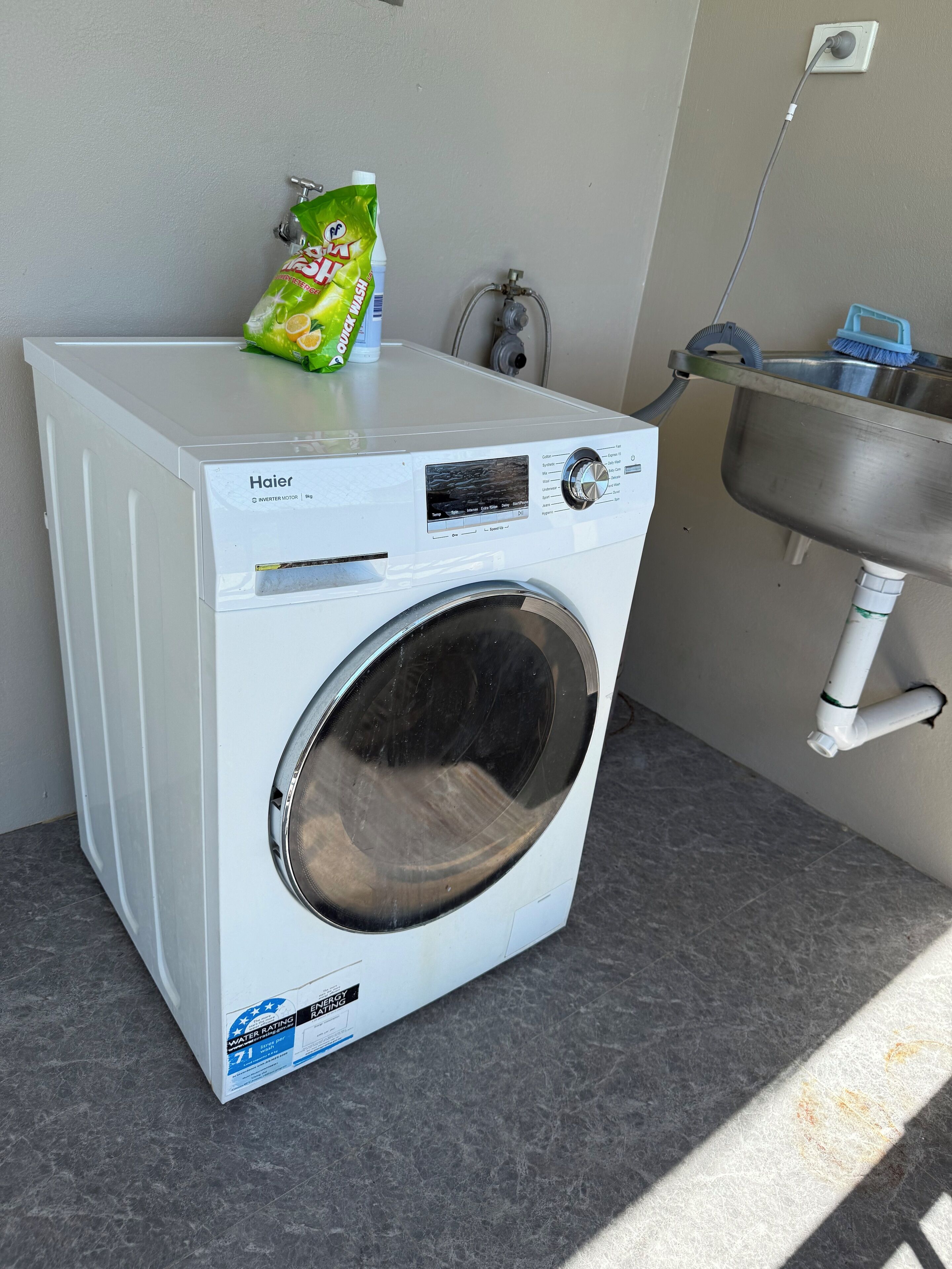 A compact, white Haier inverter motor washing machine with a front-loading door, placed on a grey countertop next to a stainless steel sink.
