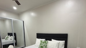 A neatly made bed with white linens and green patterned pillows, a black nightstand with a tissue box, and a ceiling fan. - Bang For Your Buck (Nadi)