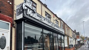 Une devanture de magasin avec une grande vitrine, une enseigne indiquant « Mother Hubbard's Fish & Chips », et une façade en briques.