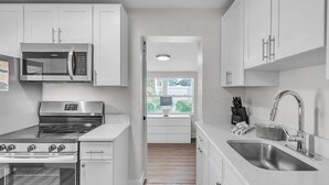 Een moderne keuken met witte kasten, roestvrijstalen apparatuur en een groot raam voor veel daglicht.