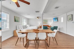 A spacious living area with a wooden dining table, white chairs, a sofa, and a ceiling fan. - The Bungalows (Treasure Island)