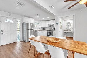 Una cucina moderna con mobili bianchi, elettrodomestici in acciaio inossidabile e un tavolo da pranzo in legno con sedie bianche.