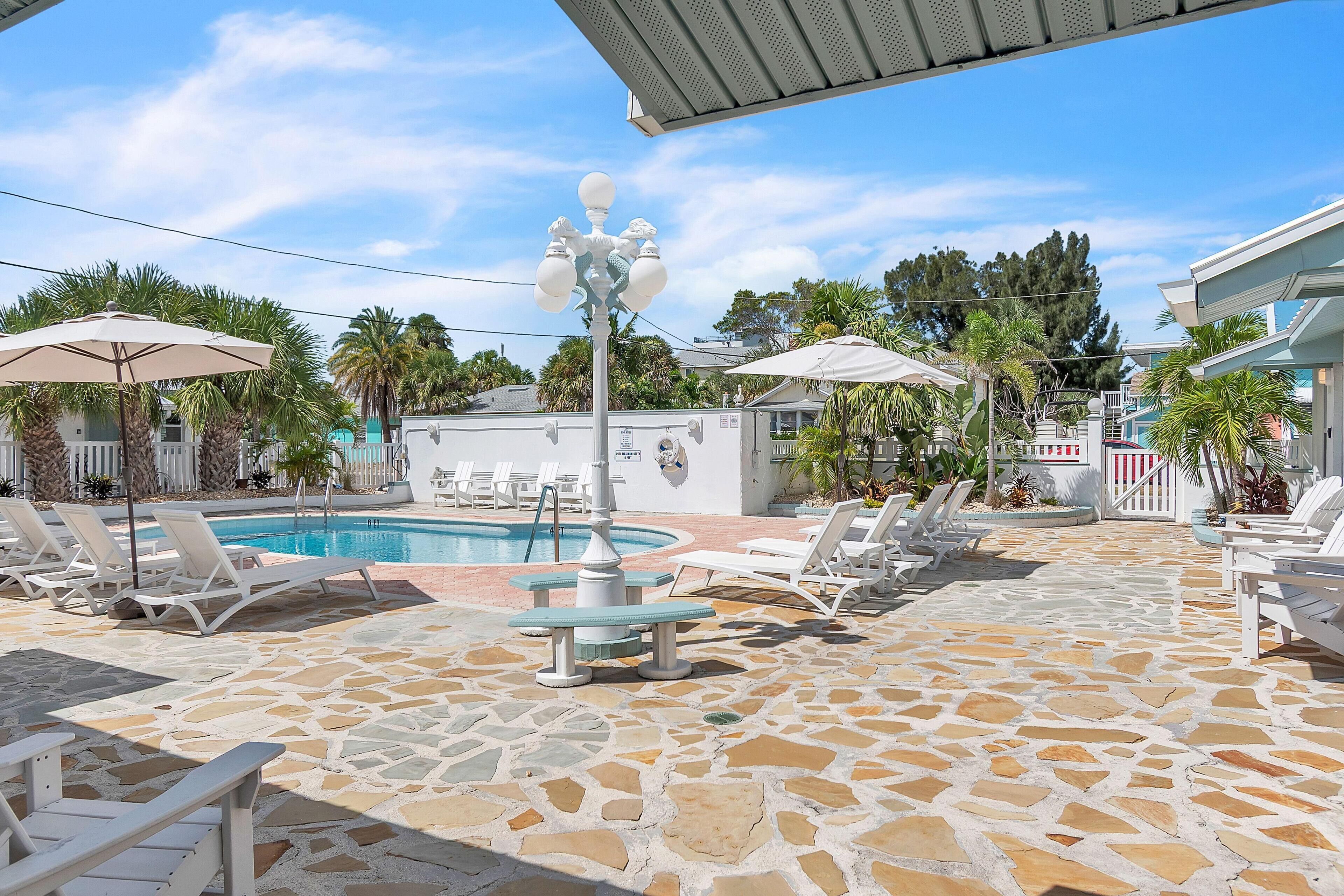Un área de piscina con sillones de descanso, sombrillas y suelo de baldosas de piedra.