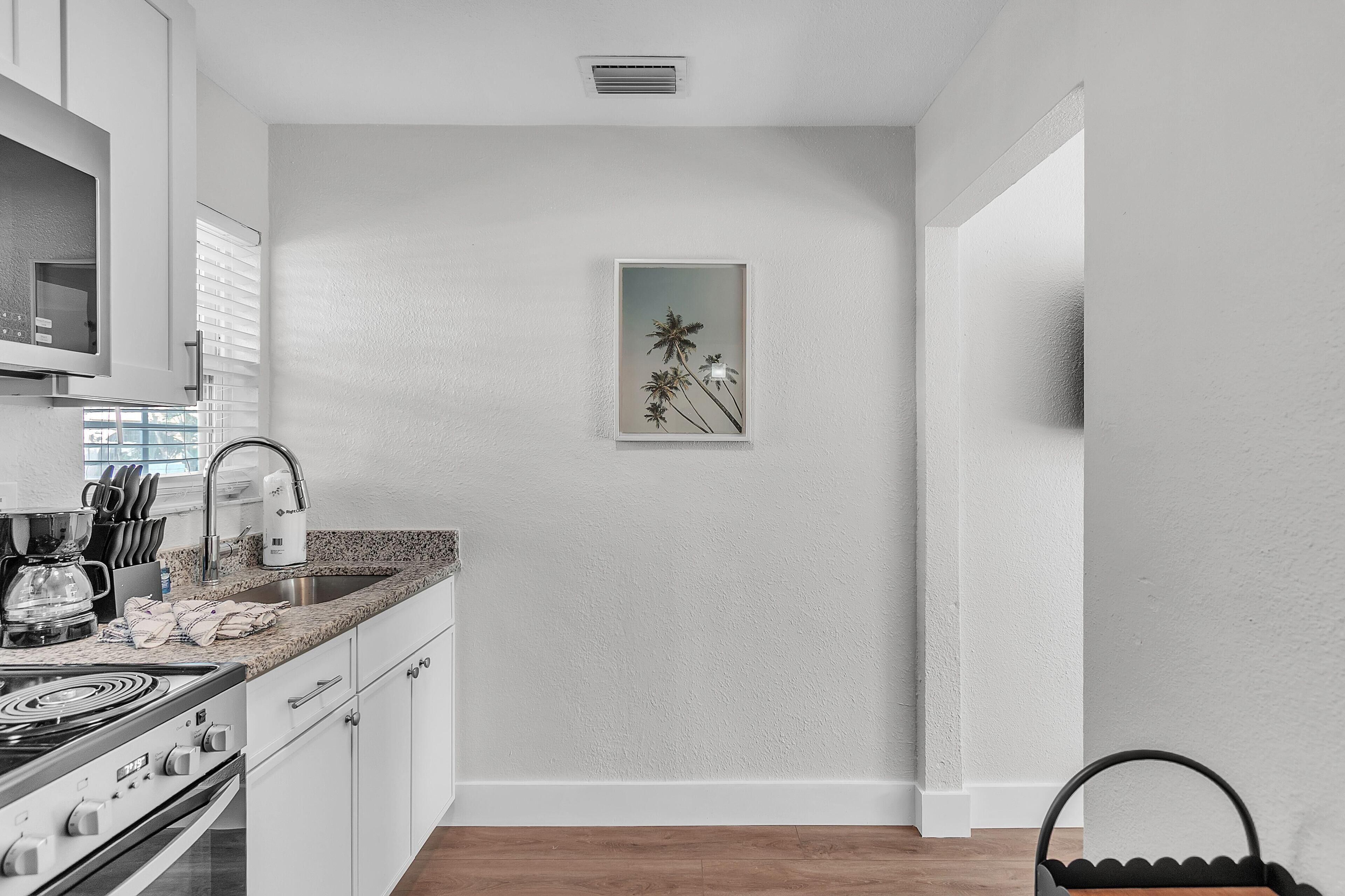 A modern kitchen with white cabinets, a granite countertop, a built-in microwave, and a coffee maker.