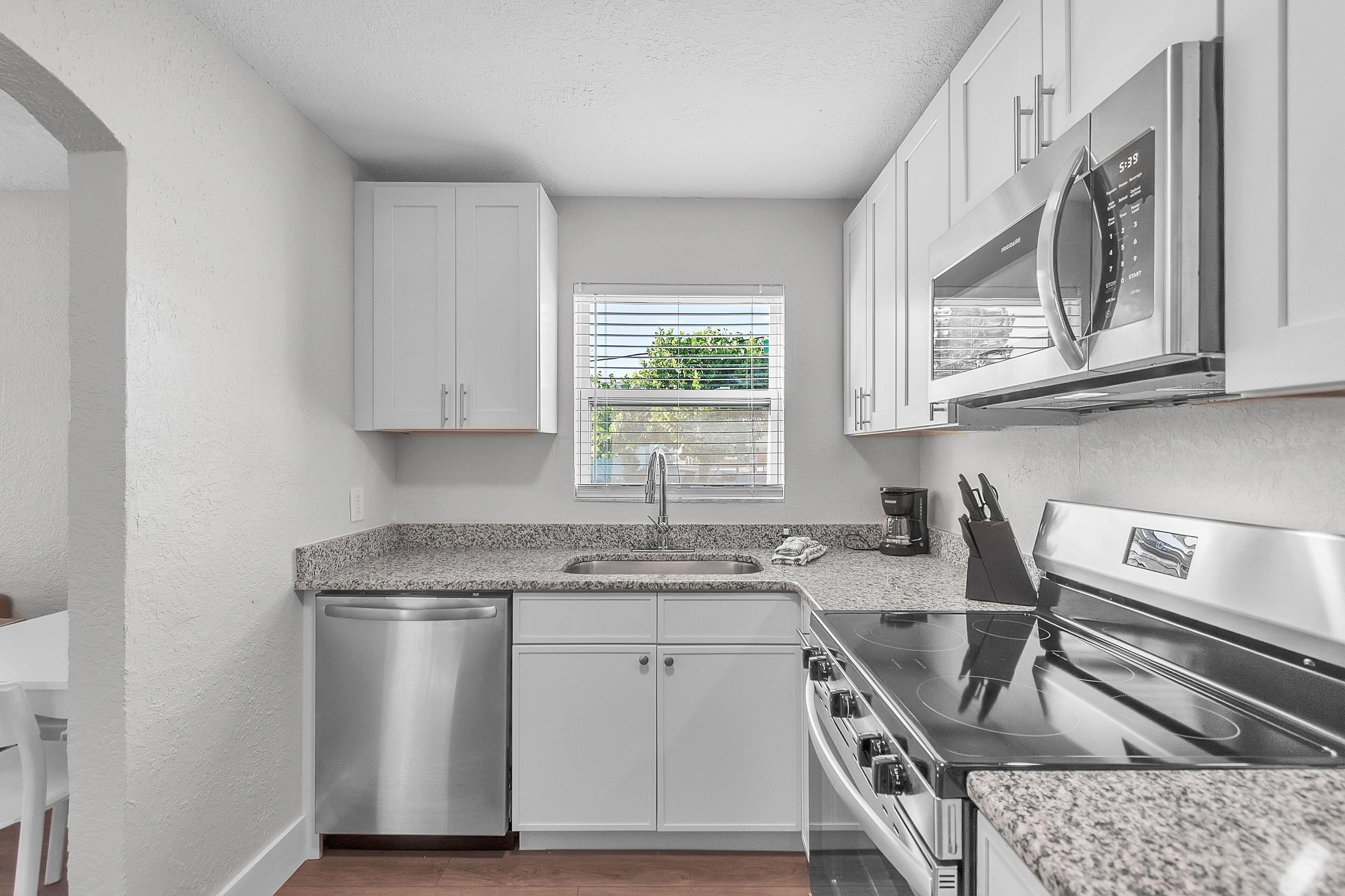 A modern kitchen with white cabinets, a stainless steel dishwasher, a built-in oven, and a microwave.