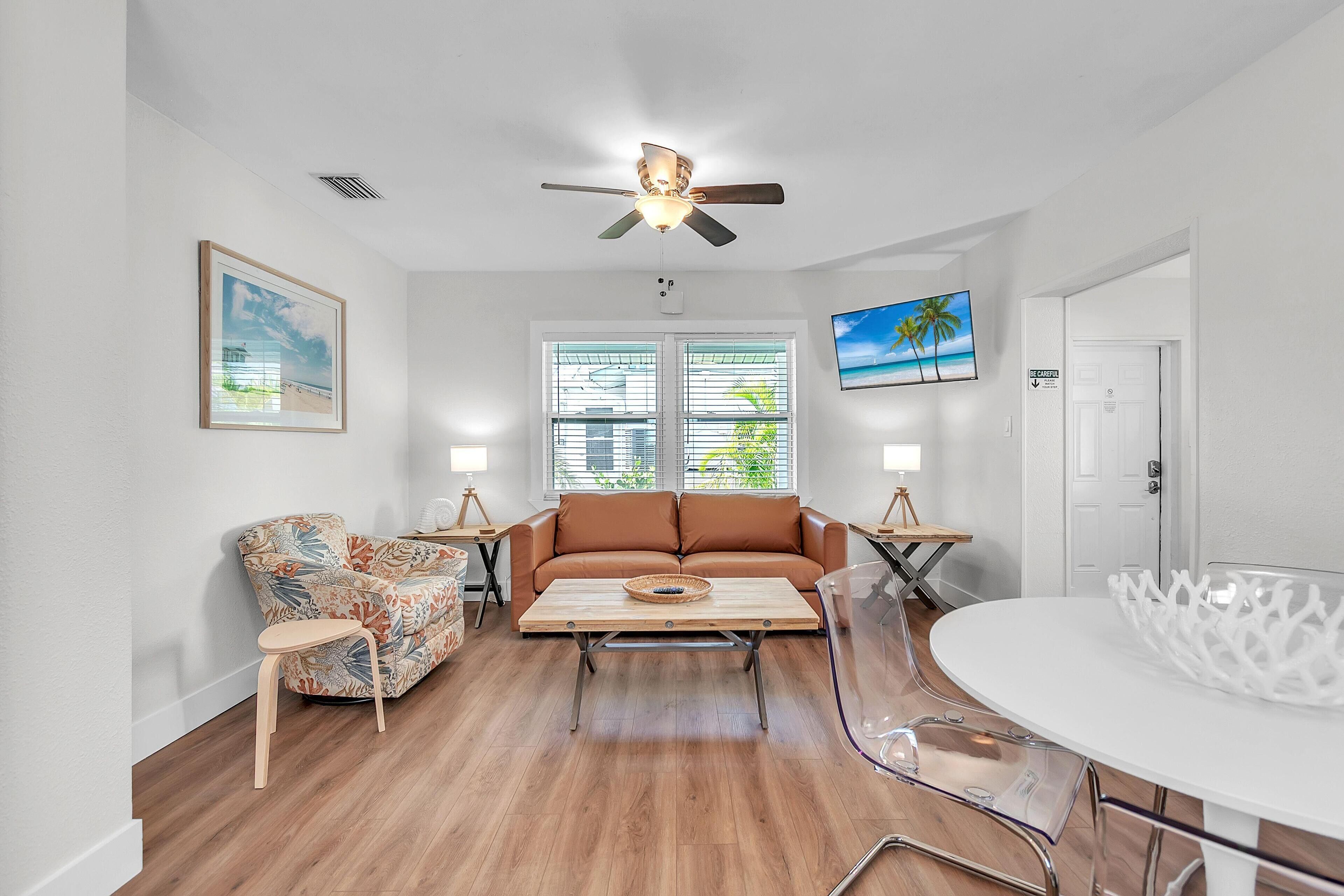 A living room with a sofa, a chair, a coffee table, a ceiling fan, and a TV.