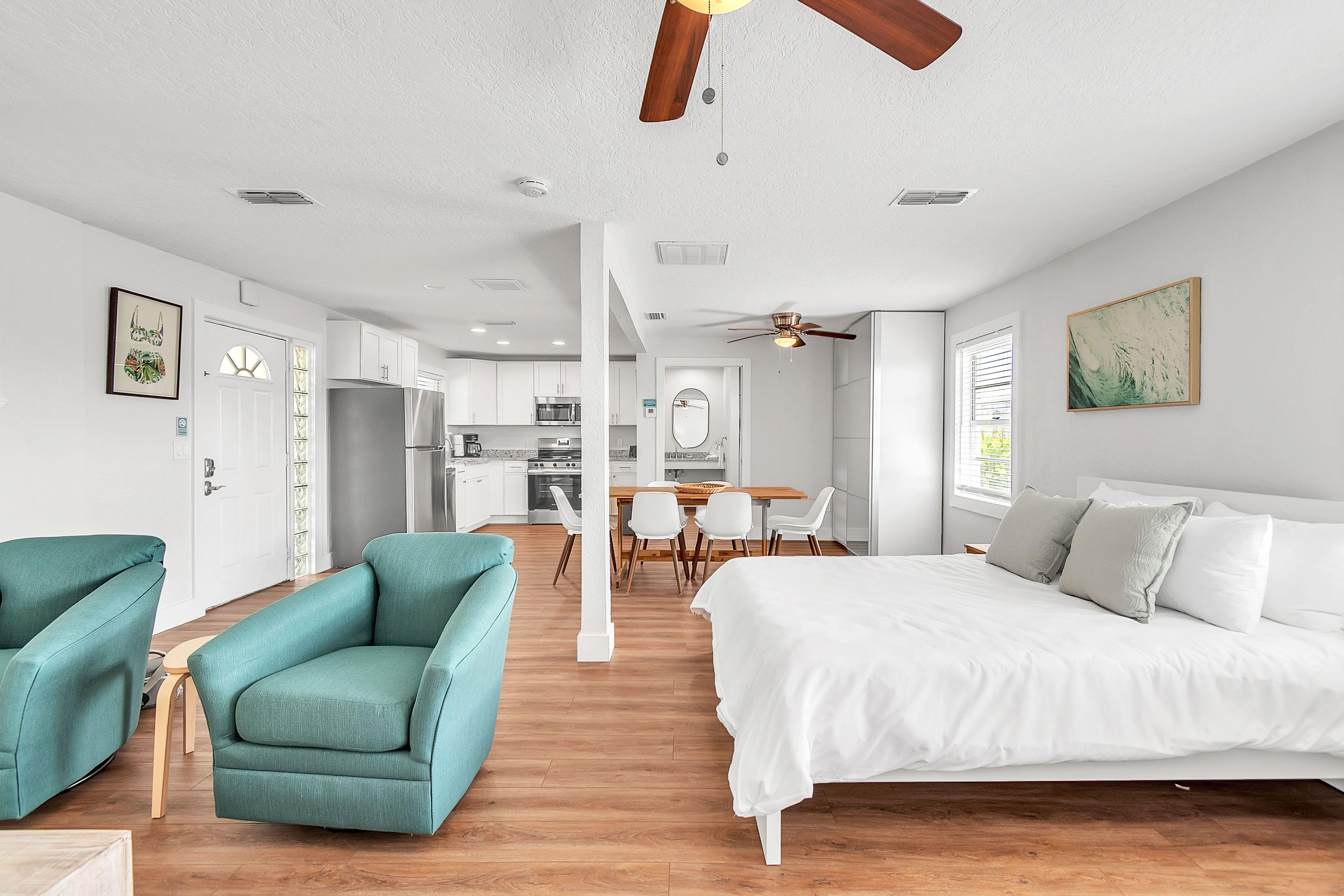 A modern bedroom with a large bed, teal armchairs, and a wooden floor.
