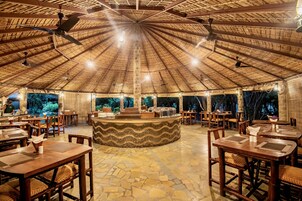 Un restaurante con techo de paja, mesas y sillas de madera, y una zona de bar central.