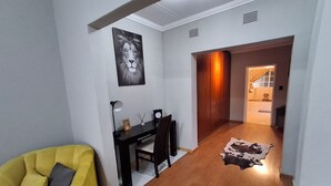 Une pièce avec un fauteuil jaune, un bureau avec une lampe, un tableau encadré et un tapis en peau de vache.