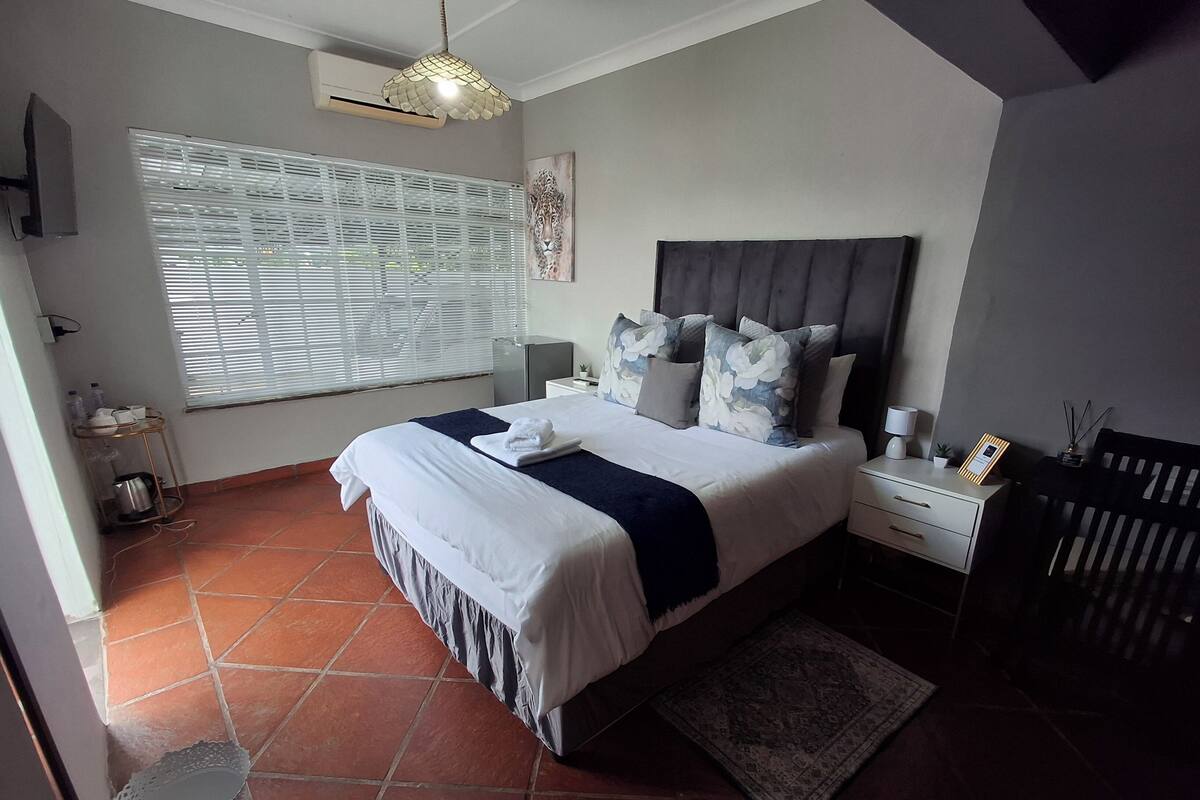 Een slaapkamer met een groot bed, een nachtkastje, een wandlamp, een ingebouwde airconditioning, een raam met zonwering en een hangende lamp.