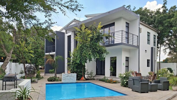 Une maison moderne à deux étages, dotée d’une piscine, de mobilier d’extérieur et d’une végétation luxuriante.