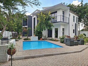 Una casa moderna de dos pisos con piscina, mobiliario exterior y abundante vegetación.
