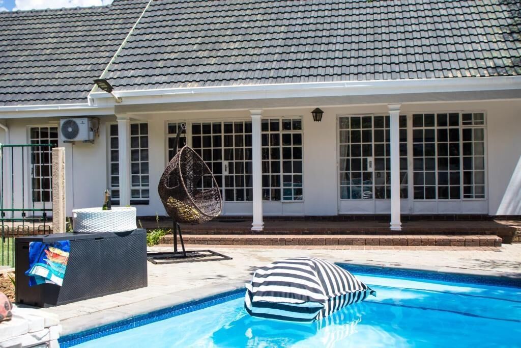 A swimming pool with a striped cushion, a wicker chair, and a white building with a tiled roof in the background.