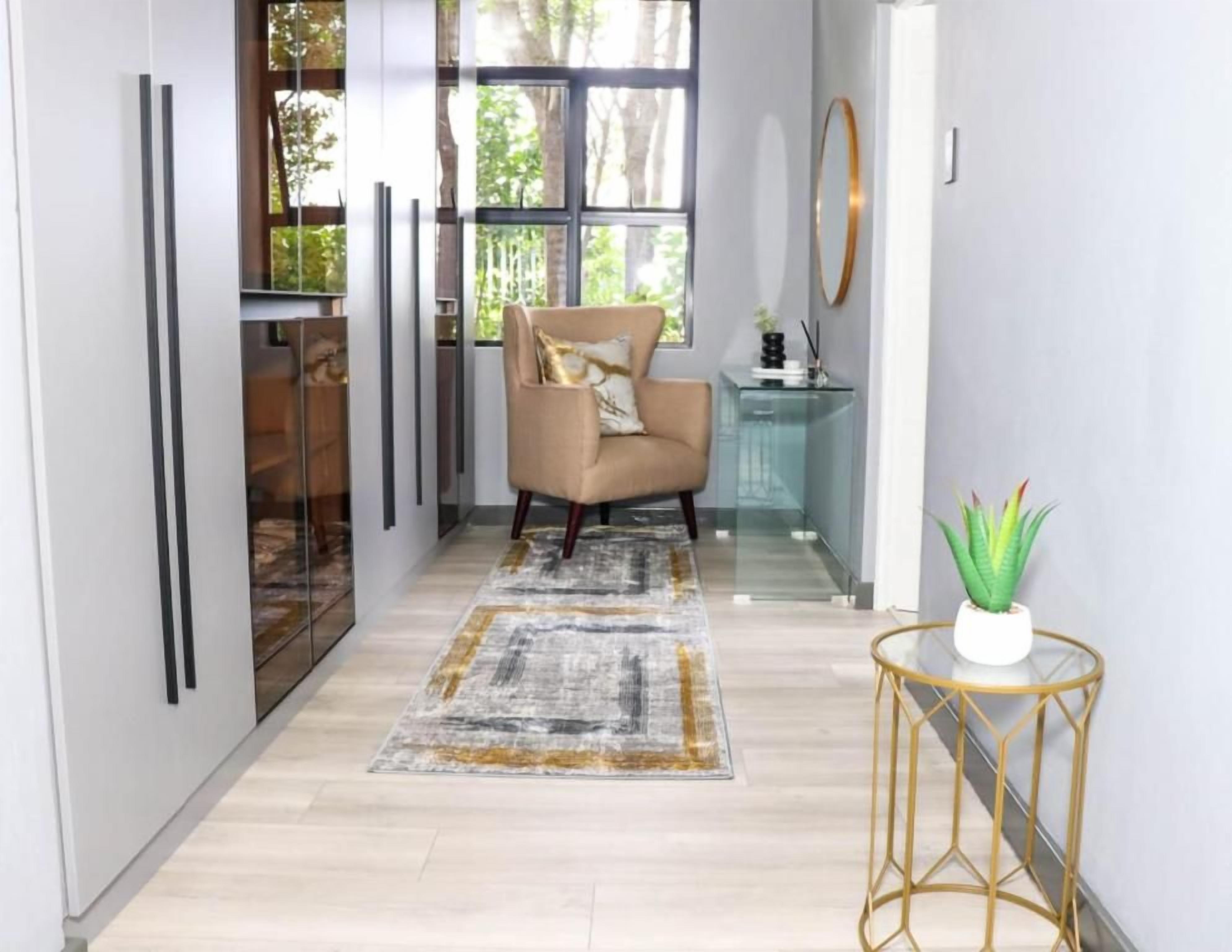 A hallway with a chair, a glass table, and a potted plant.