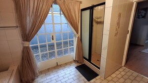 Une salle de bain avec une douche, une fenêtre avec des rideaux et un sol carrelé.