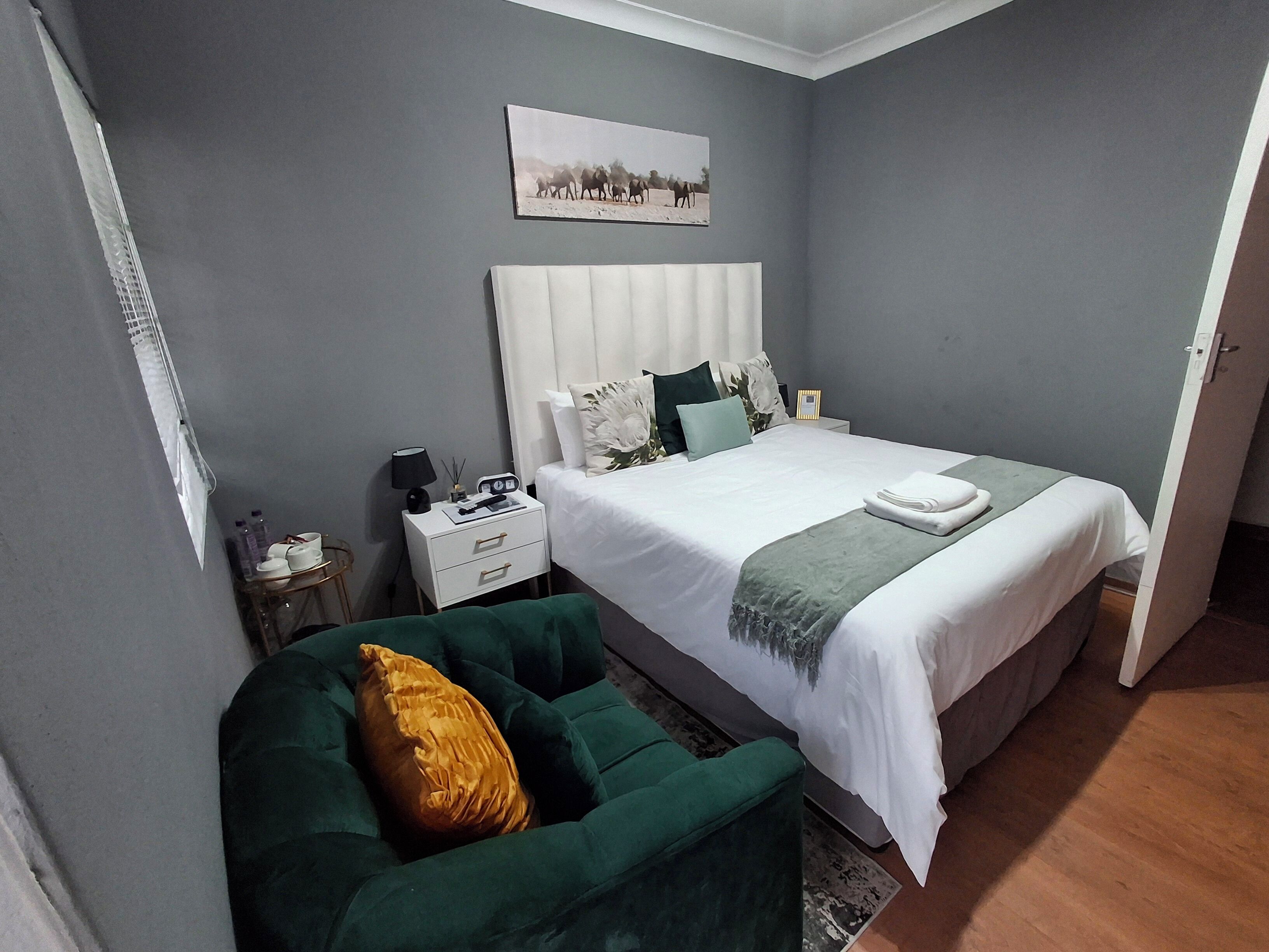 Een slaapkamer met een bed, een nachtkastje, een groene fauteuil en een aan de muur hangend schilderij.