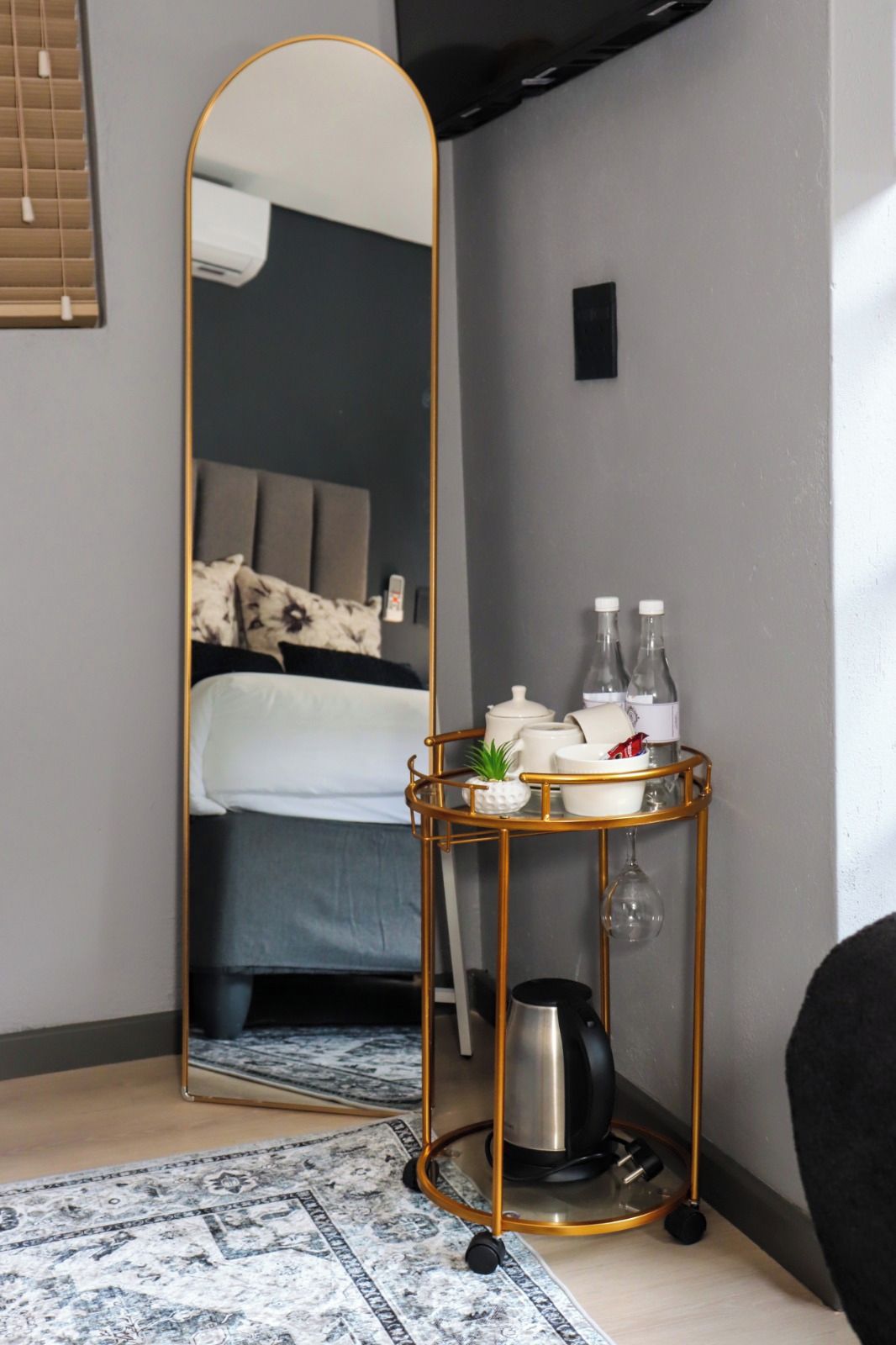 Une chambre d’hôtel avec un grand miroir, une table de chevet avec une bouilloire et un lit doté d’une tête de lit.