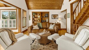 Una sala de estar acogedora con un sofá de cuero marrón, sillones blancos y una estantería de madera.