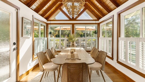 Un comedor con techo alto, vigas de madera y ventanas amplias.