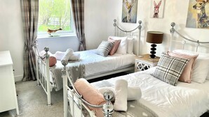 A bedroom with two beds, a bedside table, a lamp, and artwork on the walls. - Camden House Holidays Scottish Highlands Villa (Spean Bridge)