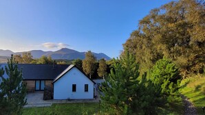 A house with a sloped roof, a small porch, and a view of mountains in the background. - Camden House Holidays Scottish Highlands Villa (Spean Bridge)