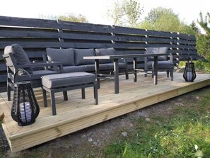 An outdoor seating area with a wooden deck, grey sofas, and black lanterns. - Camden House Holidays Scottish Highlands Villa (Spean Bridge)